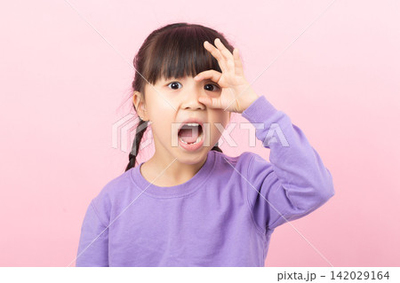 An excited young girl looking through an OK sign over her eye with a wide open mouth of surprise and joy. An excited young girl looking through an OK sign over her eye with a wide open mouth of surprise and joy. 142029164