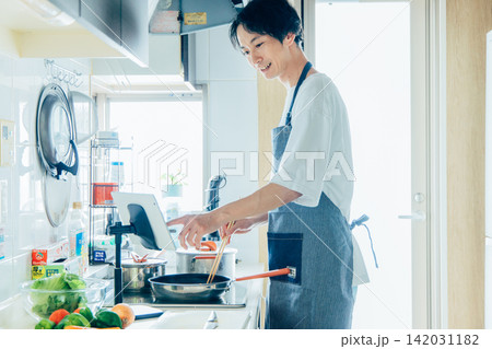 タブレットを見ながら料理をする若い男性 タブレットを見ながら料理をする若い男性 142031182