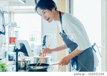 タブレットを見ながら料理をする若い男性 タブレットを見ながら料理をする若い男性 142031184