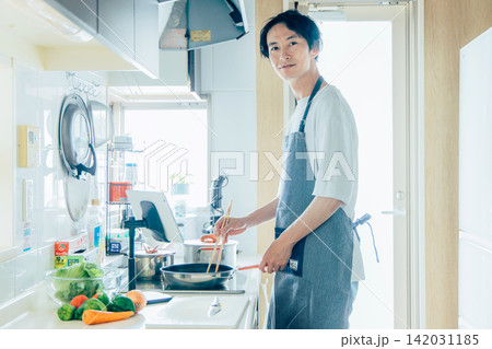 タブレットを見ながら料理をする若い男性 タブレットを見ながら料理をする若い男性 142031185
