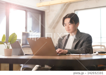 明るいオフィスでノートパソコンを操作する若い男性会社員 142032101