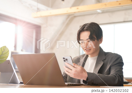 パソコン作業をしながらスマホを確認するビジネスマン パソコン作業をしながらスマホを確認するビジネスマン 142032102