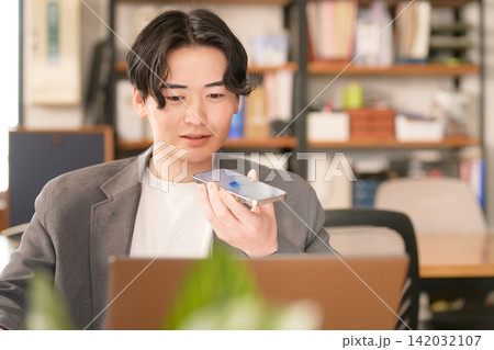 パソコン作業中にスマホの音声機能を使うビジネスマン パソコン作業中にスマホの音声機能を使うビジネスマン 142032107