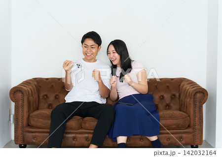 スマートフォンを見ながら熱狂する若い男女 スマートフォンを見ながら熱狂する若い男女 142032164