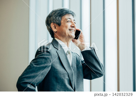 オフィスの窓際で電話をするシニアビジネスマン 142032329