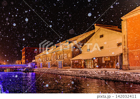 降雪の夜に暖かな光と青い灯りが運河の水面に映り込む小樽の幻想的な冬景色 142032411