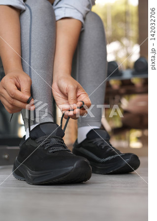 A woman ties her shoelaces ready to run at the gym. A woman ties her shoelaces ready to run at the gym. 142032706
