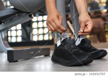 A woman ties her shoelaces ready to run at the gym. A woman ties her shoelaces ready to run at the gym. 142032707