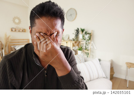 Man covering face in home setting during day Man covering face in home setting during day 142035101