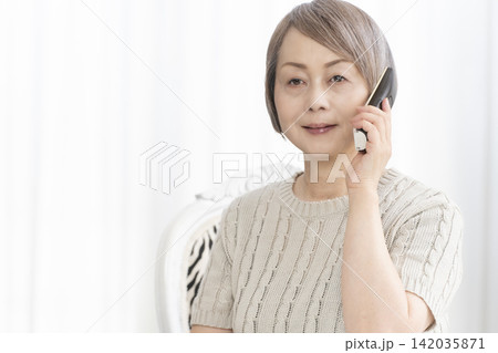 リビングで電話で喋るシニア女性 リビングで電話で喋るシニア女性 142035871