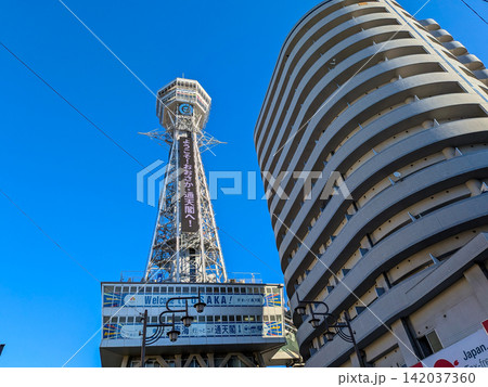 冬の澄み渡る青空にそびえ立つ大阪のランドマーク通天閣と都会のビル群 冬の澄み渡る青空にそびえ立つ大阪のランドマーク通天閣と都会のビル群 142037360