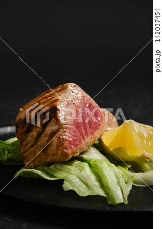 Grilled tuna steak served with lettuce and lemon on black plate Grilled tuna steak served with lettuce and lemon on black plate 142037454