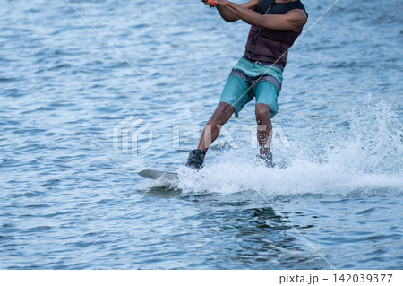 Close-up action shot of a wake boarder gliding across the water, creating a powerful spray with ample copy space Close-up action shot of a wake boarder gliding across the water, creating a powerful spray with ample copy space 142039377