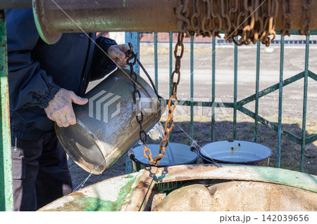 A man pours fresh cold water from a metal bucket into a basin at an old outdoor well, capturing rural life habits and the manual labor of retrieving natural resources for daily use A man pours fresh cold water from a metal bucket into a basin at an old outdoor well, capturing rural life habits and the manual labor of retrieving natural resources for daily use 142039656