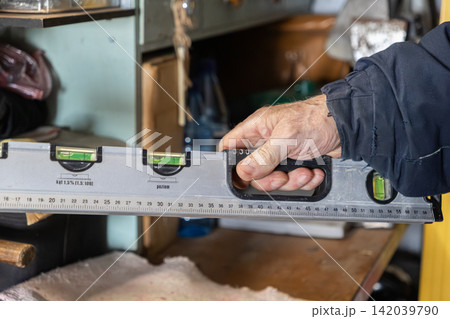A male hand holds a grey spirit level tool in a workshop setting, symbolizing precision measurement, construction accuracy, professional maintenance, and skilled manual labor tasks 142039790