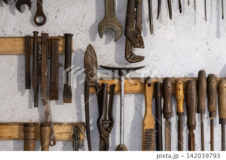 An assortment of vintage workshop tools hanging on wooden racks against a rustic white wall, representing mechanical repair services and professional craftsmanship in a classic garage An assortment of vintage workshop tools hanging on wooden racks against a rustic white wall, representing mechanical repair services and professional craftsmanship in a classic garage 142039793