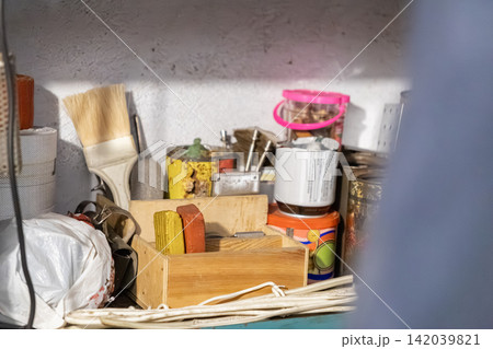 Assorted hardware and workshop supplies sit in a cluttered shelf, capturing a busy project space with paint brushes, containers and wooden boxes for organizing home repair tasks Assorted hardware and workshop supplies sit in a cluttered shelf, capturing a busy project space with paint brushes, containers and wooden boxes for organizing home repair tasks 142039821