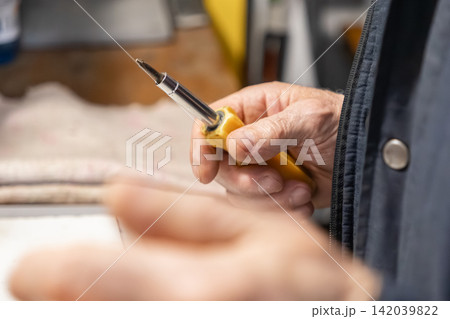 An older person holding a yellow screwdriver to perform maintenance tasks in a workshop, symbolizing skilled manual labor, home improvement projects, and a dedicated craft professional An older person holding a yellow screwdriver to perform maintenance tasks in a workshop, symbolizing skilled manual labor, home improvement projects, and a dedicated craft professional 142039822