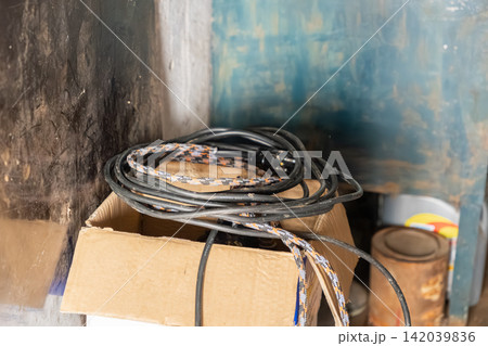Black and patterned electrical extension cables coiled neatly inside a cardboard box for organized storage, illustrating utility, workshop maintenance, and household repair management Black and patterned electrical extension cables coiled neatly inside a cardboard box for organized storage, illustrating utility, workshop maintenance, and household repair management 142039836