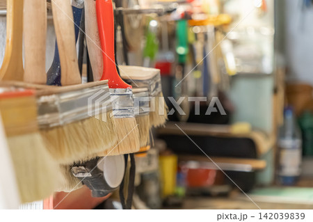 A row of various paint brushes hangs on a wall in a workshop, highlighting organized professional painting equipment ready for renovation projects and home improvement maintenance tasks A row of various paint brushes hangs on a wall in a workshop, highlighting organized professional painting equipment ready for renovation projects and home improvement maintenance tasks 142039839