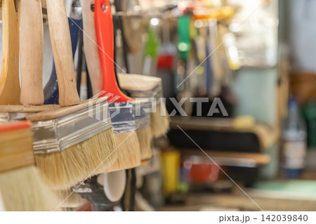 A row of various paint brushes with wooden handles hangs in a hardware store, highlighting professional renovation tools and manual craft supplies for home improvement design projects A row of various paint brushes with wooden handles hangs in a hardware store, highlighting professional renovation tools and manual craft supplies for home improvement design projects 142039840