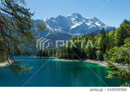 Travel landscape of Zugspitze Alps in Bavaria, Germany, scenic summer nature panorama with forest, Eibsee lake, snow mountains peak. Alpine landscape Travel landscape of Zugspitze Alps in Bavaria, Germany, scenic summer nature panorama with forest, Eibsee lake, snow mountains peak. Alpine landscape 142040560