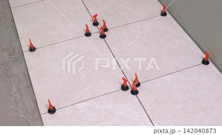 Worker Hand Laying Ceramic Tiles on the Floor. Repairman Placing White Gray Square Tiles, Applying Adhesive. Builder Installing Tile Using Leveler, Tile Leveling Clips. Tiling. Finishing Repair Work. Worker Hand Laying Ceramic Tiles on the Floor. Repairman Placing White Gray Square Tiles, Applying Adhesive. Builder Installing Tile Using Leveler, Tile Leveling Clips. Tiling. Finishing Repair Work. 142040873