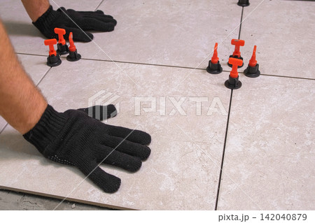Worker Hand Laying Ceramic Tiles on the Floor. Repairman Placing White Gray Square Tiles, Applying Adhesive. Builder Installing Tile Using Leveler, Tile Leveling Clips. Tiling. Finishing Repair Work. Worker Hand Laying Ceramic Tiles on the Floor. Repairman Placing White Gray Square Tiles, Applying Adhesive. Builder Installing Tile Using Leveler, Tile Leveling Clips. Tiling. Finishing Repair Work. 142040879