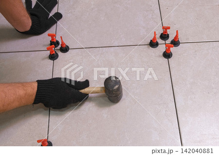 Worker Hand Laying Ceramic Tiles on the Floor. Repairman Placing White Gray Square Tiles, Applying Adhesive. Builder Installing Tile Using Leveler, Tile Leveling Clips. Tiling. Finishing Repair Work. Worker Hand Laying Ceramic Tiles on the Floor. Repairman Placing White Gray Square Tiles, Applying Adhesive. Builder Installing Tile Using Leveler, Tile Leveling Clips. Tiling. Finishing Repair Work. 142040881