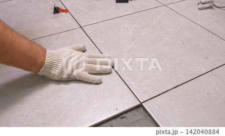 Worker Hand Laying Ceramic Tiles on the Floor. Repairman Placing White Gray Square Tiles, Applying Adhesive. Builder Installing Tile Using Leveler, Tile Leveling Clips. Tiling. Finishing Repair Work. Worker Hand Laying Ceramic Tiles on the Floor. Repairman Placing White Gray Square Tiles, Applying Adhesive. Builder Installing Tile Using Leveler, Tile Leveling Clips. Tiling. Finishing Repair Work. 142040884