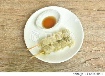 Chinese dumpling stuffed mashed pork stabbing wooden stick dipping soy sauce on plate Chinese dumpling stuffed mashed pork stabbing wooden stick dipping soy sauce on plate 142041049