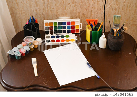 Art space includes a chair, chalkboard, easel, and plant in a room with plain walls and wooden floor Art space includes a chair, chalkboard, easel, and plant in a room with plain walls and wooden floor 142041562