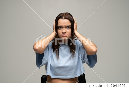 Young woman covering ears, feeling annoyed and stressed by loud noise, experiencing headache and frustration Young woman covering ears, feeling annoyed and stressed by loud noise, experiencing headache and frustration 142041661