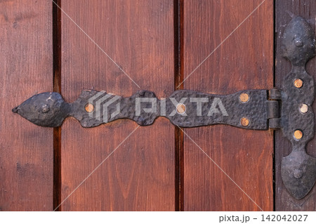 Ornate dark metal hinge securing a weathered brown wooden door, showcasing handcrafted hardware and traditional craftsmanship, reflecting history and vintage style 142042027