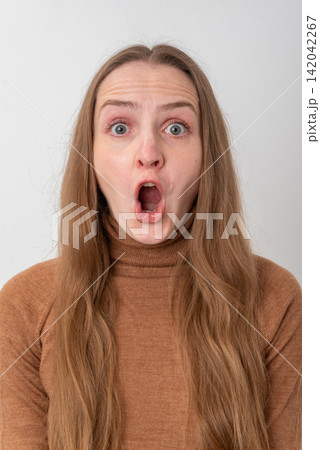 Young woman gasping in shock with mouth open wide, dramatic surprised expression and wide eyes against a clean white studio background, headshot portrait, isolated emotion Young woman gasping in shock with mouth open wide, dramatic surprised expression and wide eyes against a clean white studio background, headshot portrait, isolated emotion 142042267