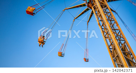 Chain swing carousel amusement ride with people against blue sky, outdoor fun and entertainment concept Chain swing carousel amusement ride with people against blue sky, outdoor fun and entertainment concept 142042371