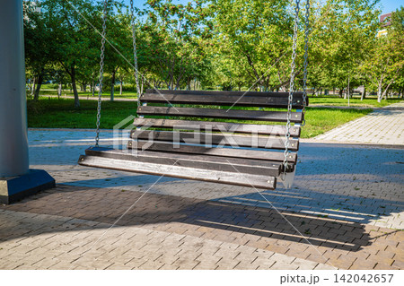 Wooden park bench swing hanging on metal chains in summer city park Wooden park bench swing hanging on metal chains in summer city park 142042657