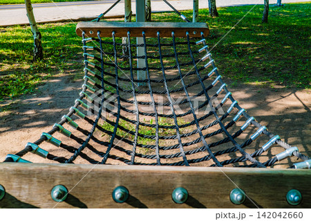 Close up of rope net hammock swing seat with metal bolt on ground in summer park, outdoor recreation concept Close up of rope net hammock swing seat with metal bolt on ground in summer park, outdoor recreation concept 142042660