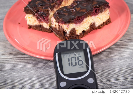Glucose meter with result of sugar level and fresh cheesecake with cherries and chocolate 142042789