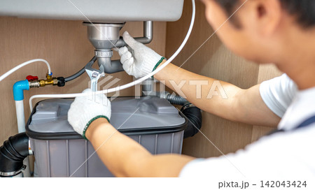 Male plumber with glove fixing pipe connection under kitchen sink with adjustable wrench Male plumber with glove fixing pipe connection under kitchen sink with adjustable wrench 142043424