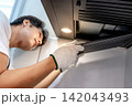 Asian male technician removing range metal filter looking at extractor motor inside the cooker hood 142043493