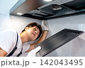 Asian male technician removing range metal filter looking at extractor motor inside the cooker hood 142043495