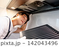 Asian male technician removing range metal filter looking at extractor motor inside the cooker hood 142043496