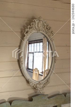 Vintage oval mirror with ornate carved frame hanging on wooden wall indoors 142044680