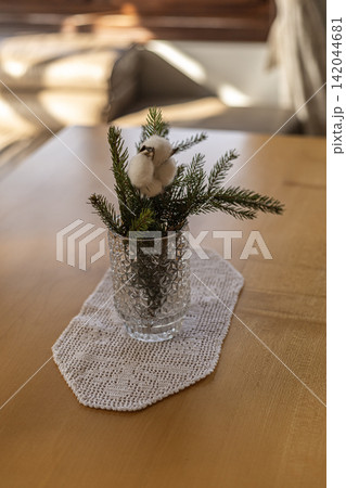 Fir branch with cotton flower in textured glass vase on wooden table Fir branch with cotton flower in textured glass vase on wooden table 142044681
