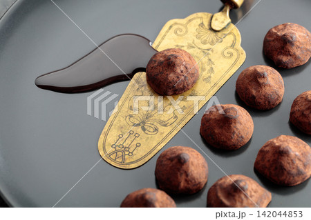 Chocolate truffles, chocolate sauce, and vintage brass cake server on a black plate. 142044853
