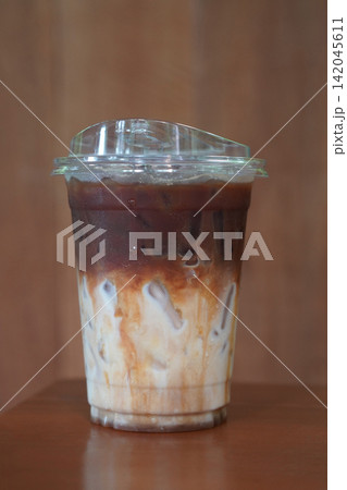 front view closeup cool and ice coffee and caramel Macchiato drink in a clear plastic cup, on wooden floor, brown wooden wall background, drink, cool, copy space 142045611
