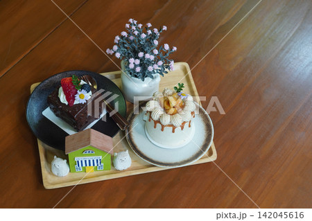 top view macadamia coffee cake and chocolate cake in ceramic plates and vase of pink flowers and decorative on a wooden tray placed on a wooden floor background, food, sweet, copy space top view macadamia coffee cake and chocolate cake in ceramic plates and vase of pink flowers and decorative on a wooden tray placed on a wooden floor background, food, sweet, copy space 142045616