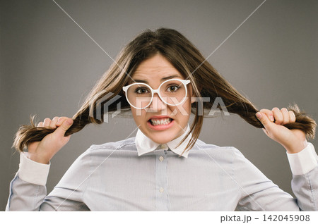 Woman, portrait and pulling hair in studio with stress for education, exam or assessment by background. Girl, college student or frustrated person with anxiety for study, test or glasses for learning Woman, portrait and pulling hair in studio with stress for education, exam or assessment by background. Girl, college student or frustrated person with anxiety for study, test or glasses for learning 142045908
