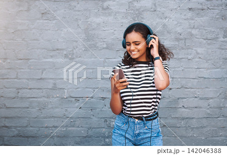 Girl, headphones and cellphone with wall background for music listening, subscription or podcast. Female person, smile and urban city with technology for entertainment with playlist, app or mockup 142046388